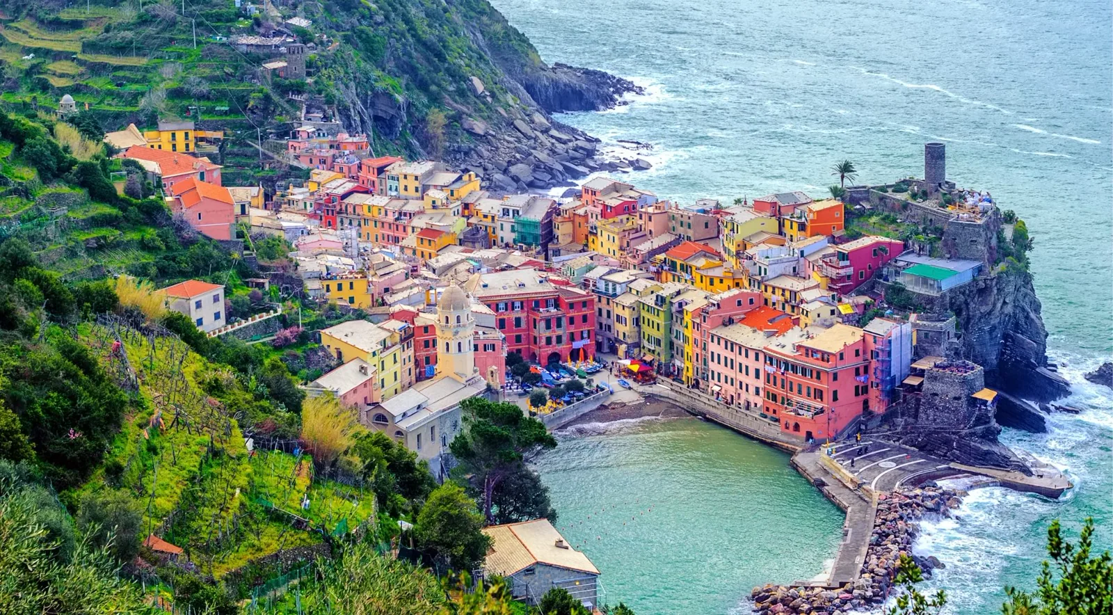Aerial view of Vernazza — the coloured houses curling around the harbour inlet seen from the castle trail